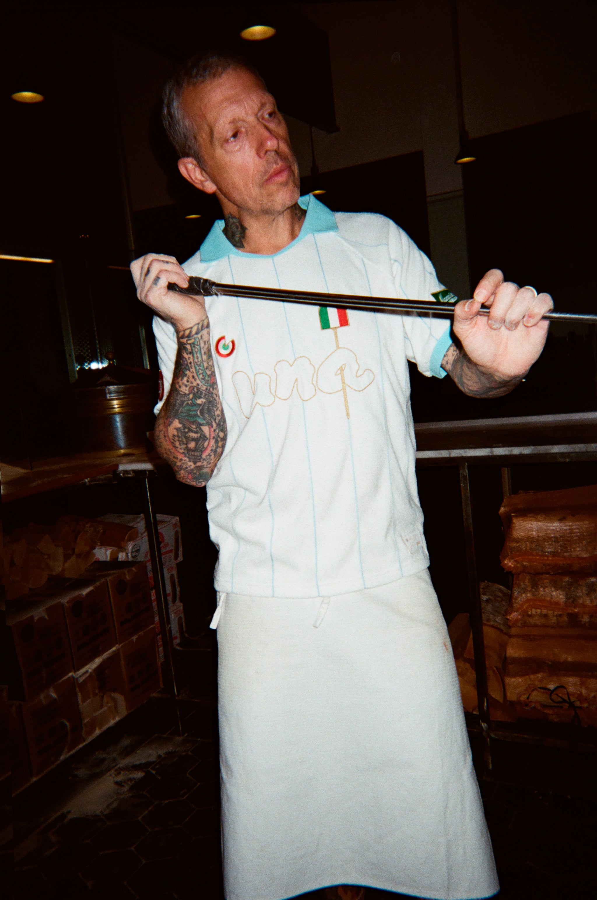 A man wearing a white pizza jersey with a light blue collar and a white apron over it.
