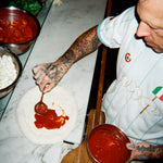 Bird's eye view image of a chef adding sauce to pizza dough.