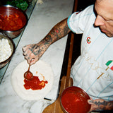 Bird's eye view image of a chef adding sauce to pizza dough.
