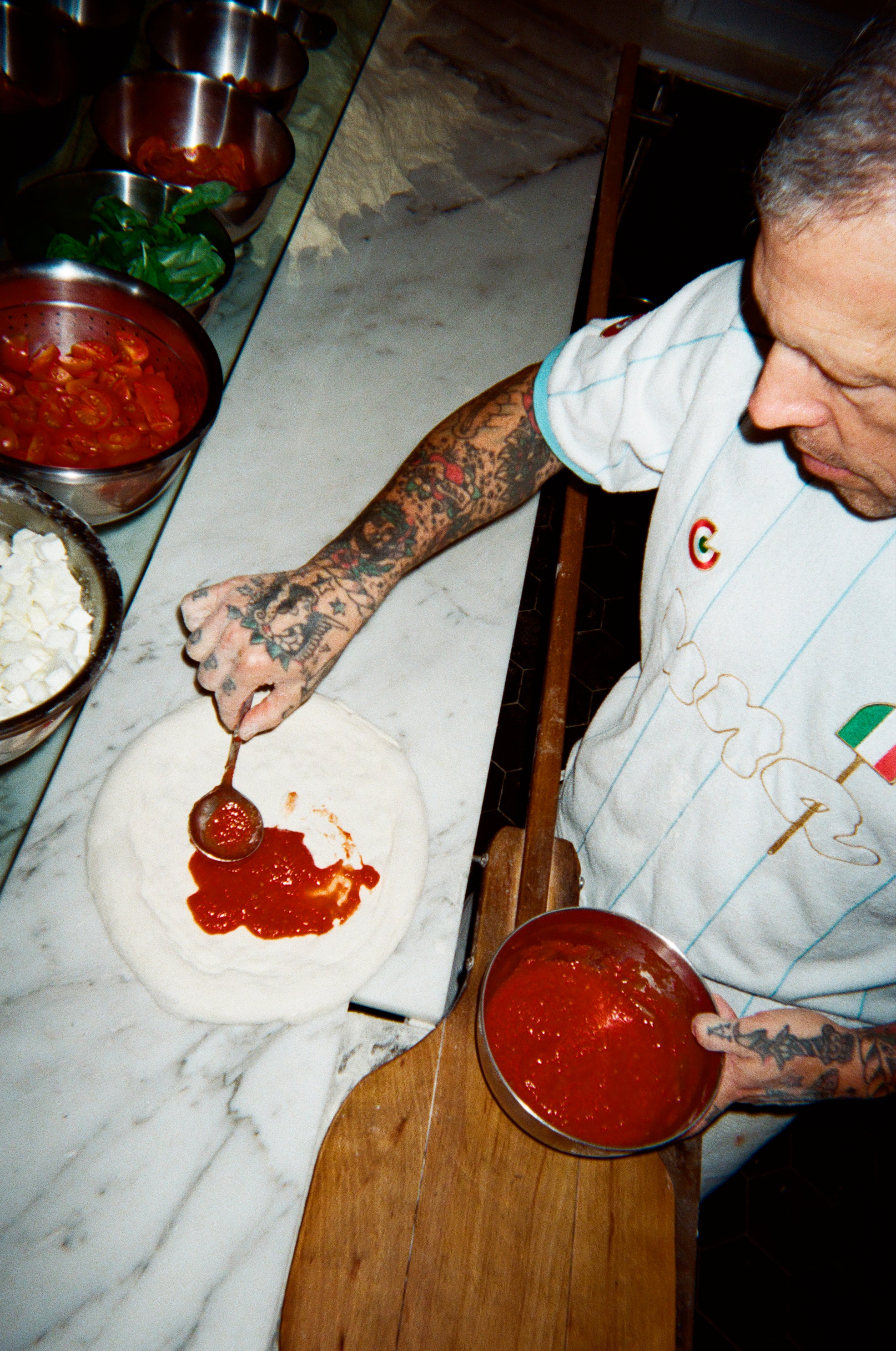 Bird's eye view image of a chef adding sauce to pizza dough.