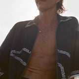Brunette man wearing the black short-sleeve terrycloth 'Beach Break' Cabana fully unzipped, shown from the waist up.