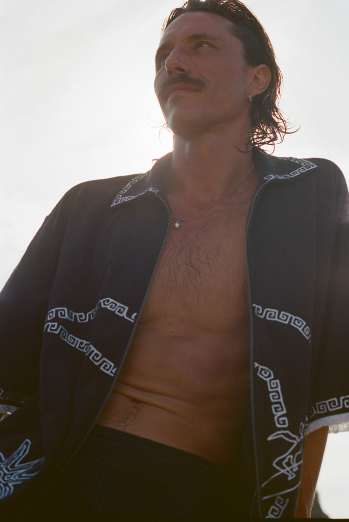 Brunette man wearing the black short-sleeve terrycloth 'Beach Break' Cabana fully unzipped, shown from the waist up.