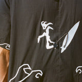 Close-up image of the embroidered surfer, attached to his board with an ankle leash. The ankle leash appears as a small loop to button the shirt.
