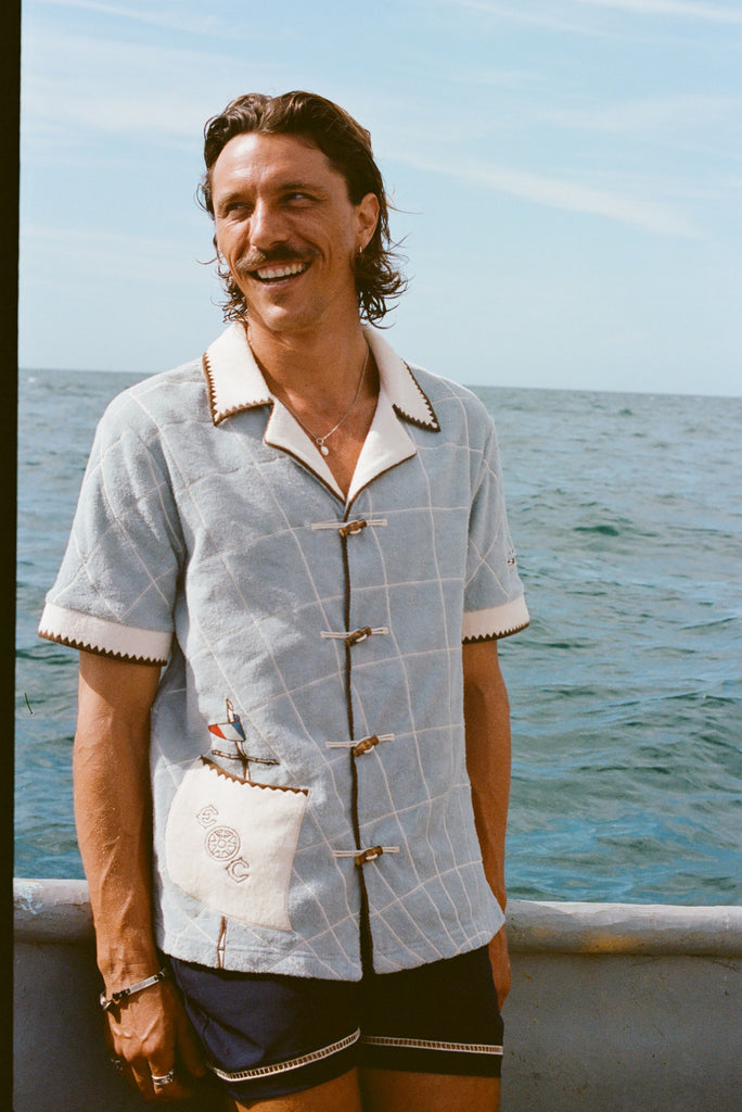 Male model smiling on boat, wearing 'The Explorers Club' Expedition Cabana and swim trunks.