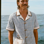 Male model smiling on boat, wearing 'The Explorers Club' Expedition Cabana and swim trunks.