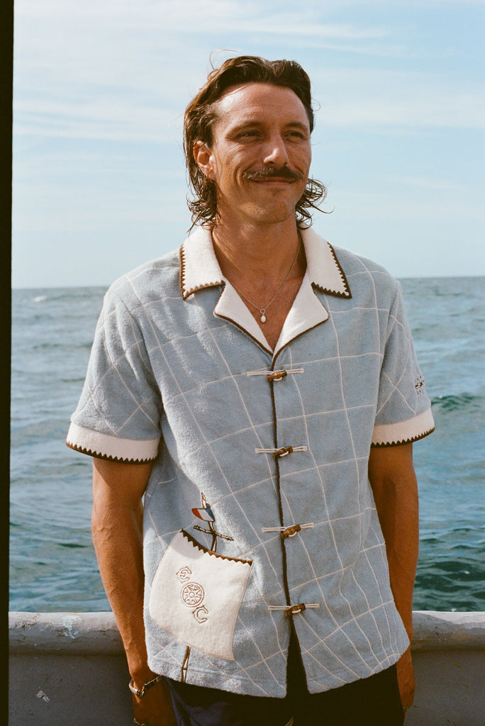 Male model smiling on boat, wearing 'The Explorers Club' Expedition Cabana and swim trunks.