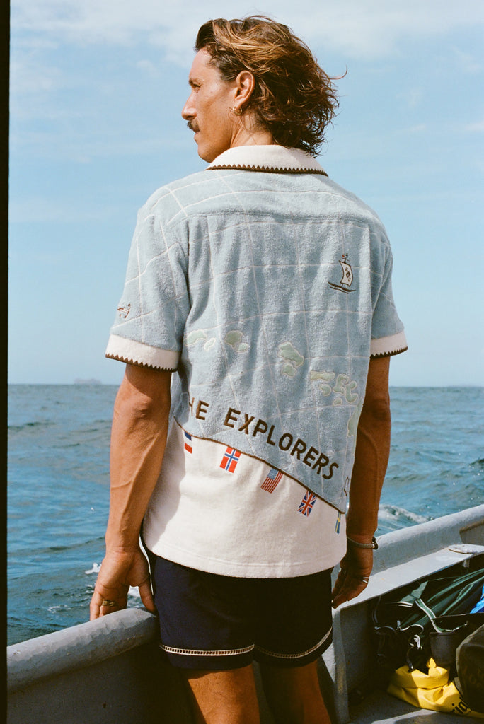 Male Model with long hang is showing off the backside of 'The Explorers Club' Expedition Cabana with swim trunks on a boat.