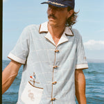 Male model wearing 'The Explorers Club' 6-Panel Souvenir Cap (Wool) with 'The Explorers Club' Expedition Cabana, leaning on the side of a boat in the water.