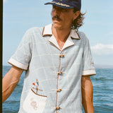 Male model wearing 'The Explorers Club' 6-Panel Souvenir Cap (Wool) with 'The Explorers Club' Expedition Cabana, leaning on the side of a boat in the water.