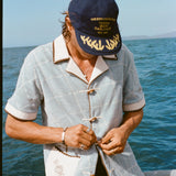 Male model wearing 'The Explorers Club' 6-Panel Souvenir Cap (Wool) and buttoning up his 'The Explorers Club' Expedition Cabana.