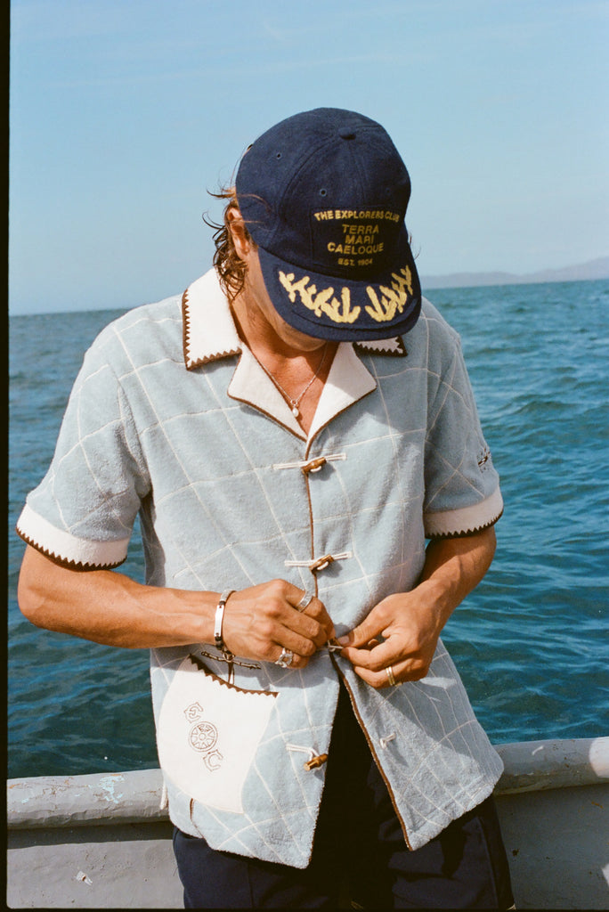Male model wearing 'The Explorers Club' 6-Panel Souvenir Cap (Wool) and buttoning up his 'The Explorers Club' Expedition Cabana.