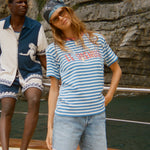 Woman in a striped shirt and denim shorts sitting on a boat with a man in the background.