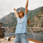 Woman standing on a boat wearing the blue striped Le Sirenuse terry cloth t-shirt.