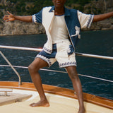 Person standing on a boat with arms outstretched, wearing a blue and white Late Checkout Cabana set. 