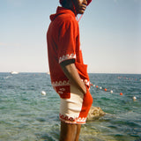 Person wearing a red Le Sirenuse shirt and hat standing on a rock in front of the ocean. 