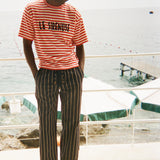 Person wearing a red and white striped shirt with 'Le Sirenuse' embroidered, and black and white striped pants standing on a deck.