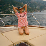 Woman in a striped Le Sirenuse shirt and sunglasses on a boat with a scenic background