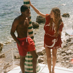 Two people in Le Sirenuse red, standing in front of a rocky beach with ocean in the background.