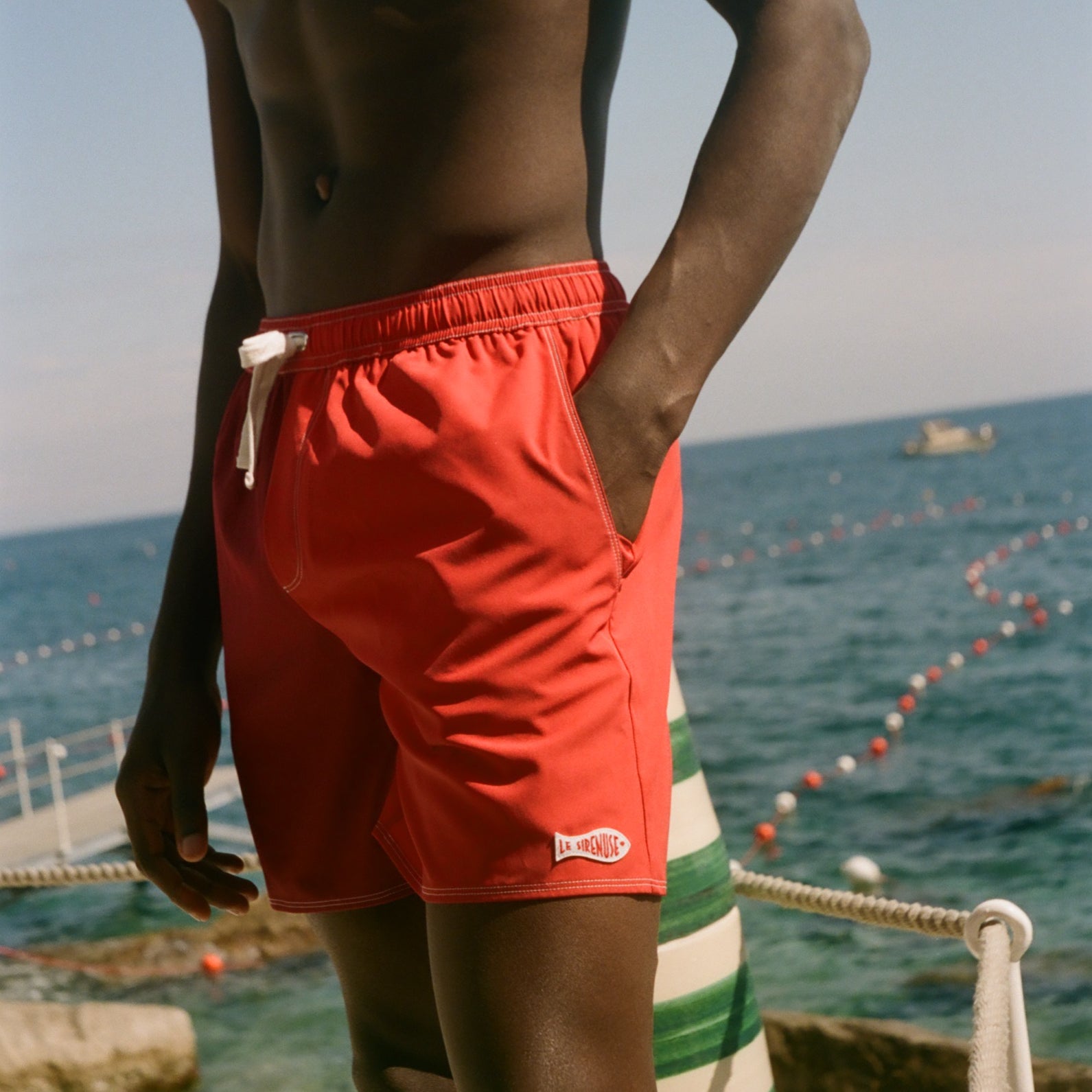 Person wearing red swim shorts standing on a beach with ocean view