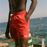 Person wearing red swim shorts standing on a beach with ocean view