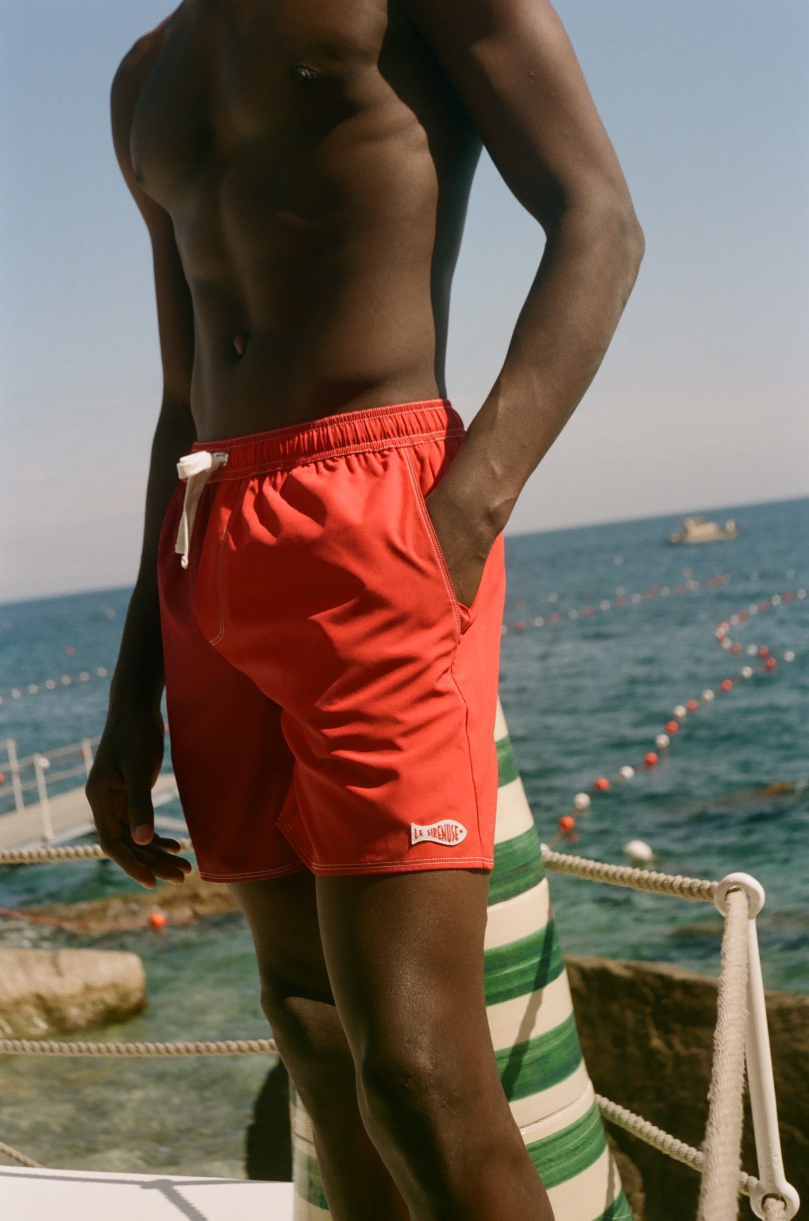 Person wearing red swim shorts standing on a beach with ocean view