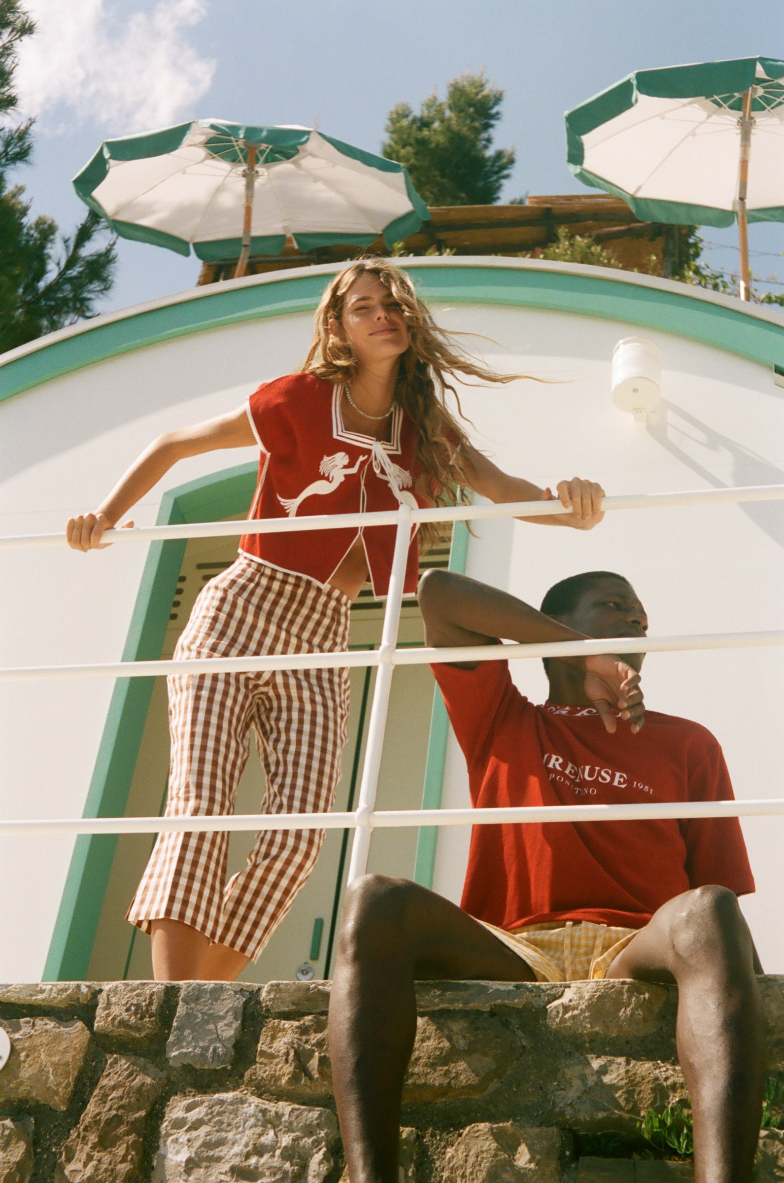 Two people standing by a scenic ocean view, wearing shirts from the Le Sirenuse x Tombolo collaboration.