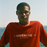 Person wearing a red 'Le Sirenuse Positano' t-shirt with ocean in the background