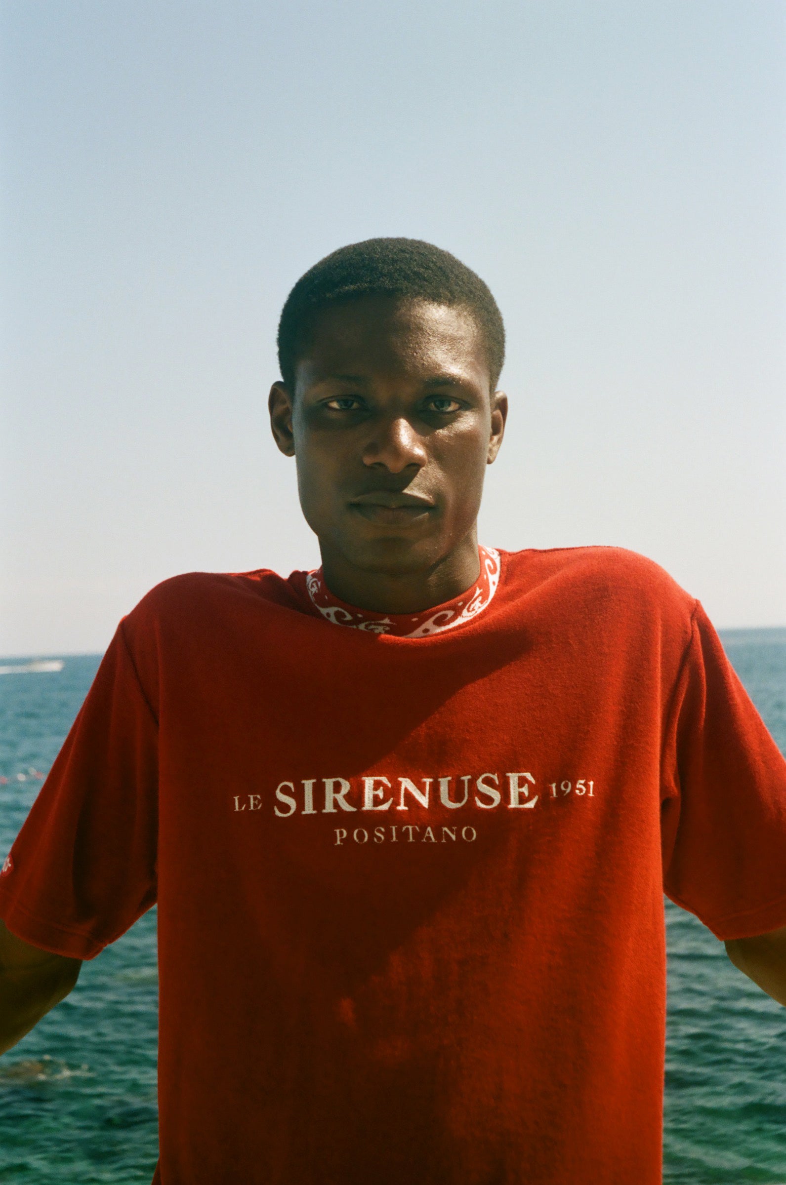 Person wearing a red 'Le Sirenuse Positano' t-shirt with ocean in the background
