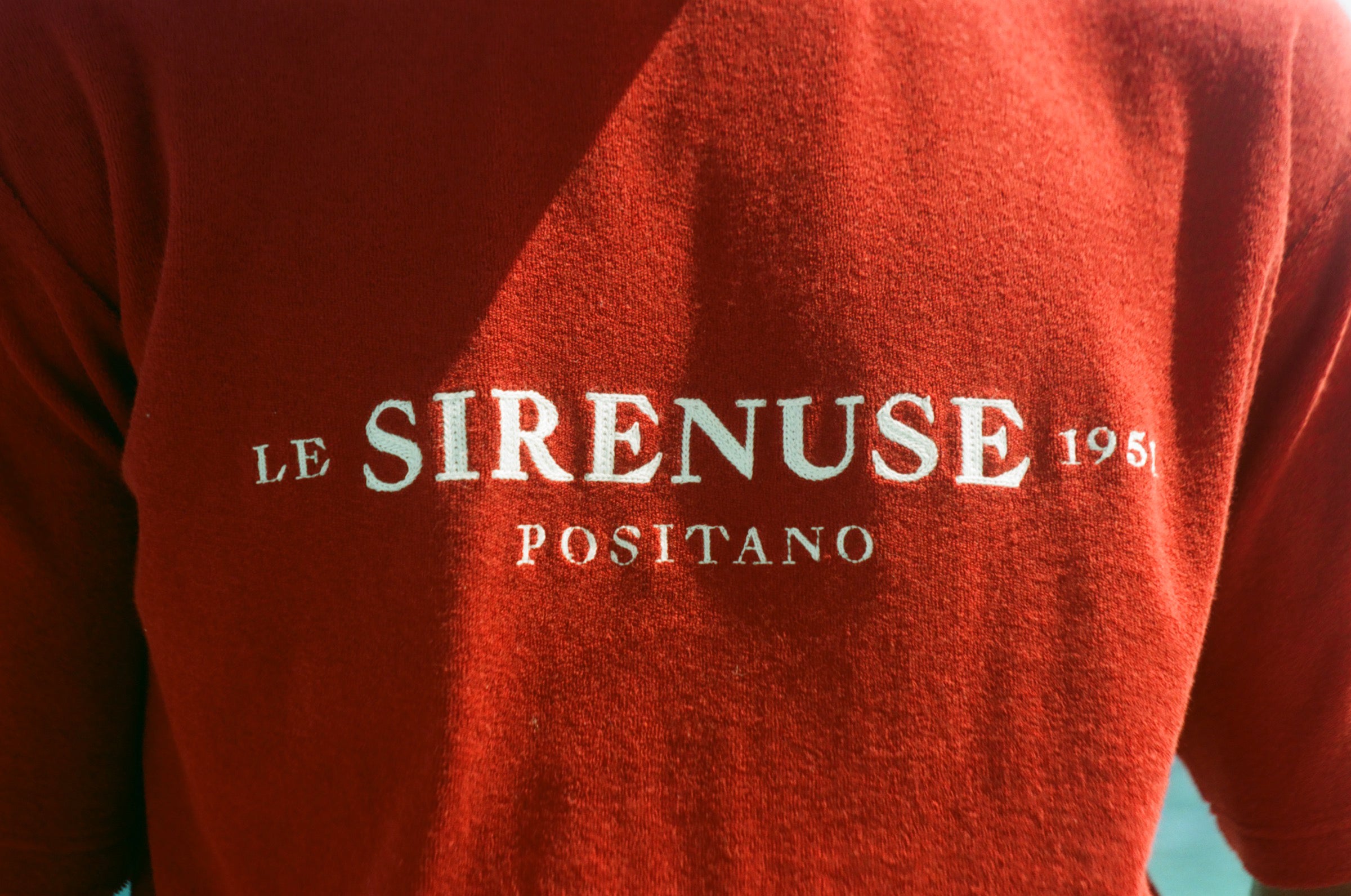 Red garment with 'Le Sirenuse Positano' branding on a blurred background