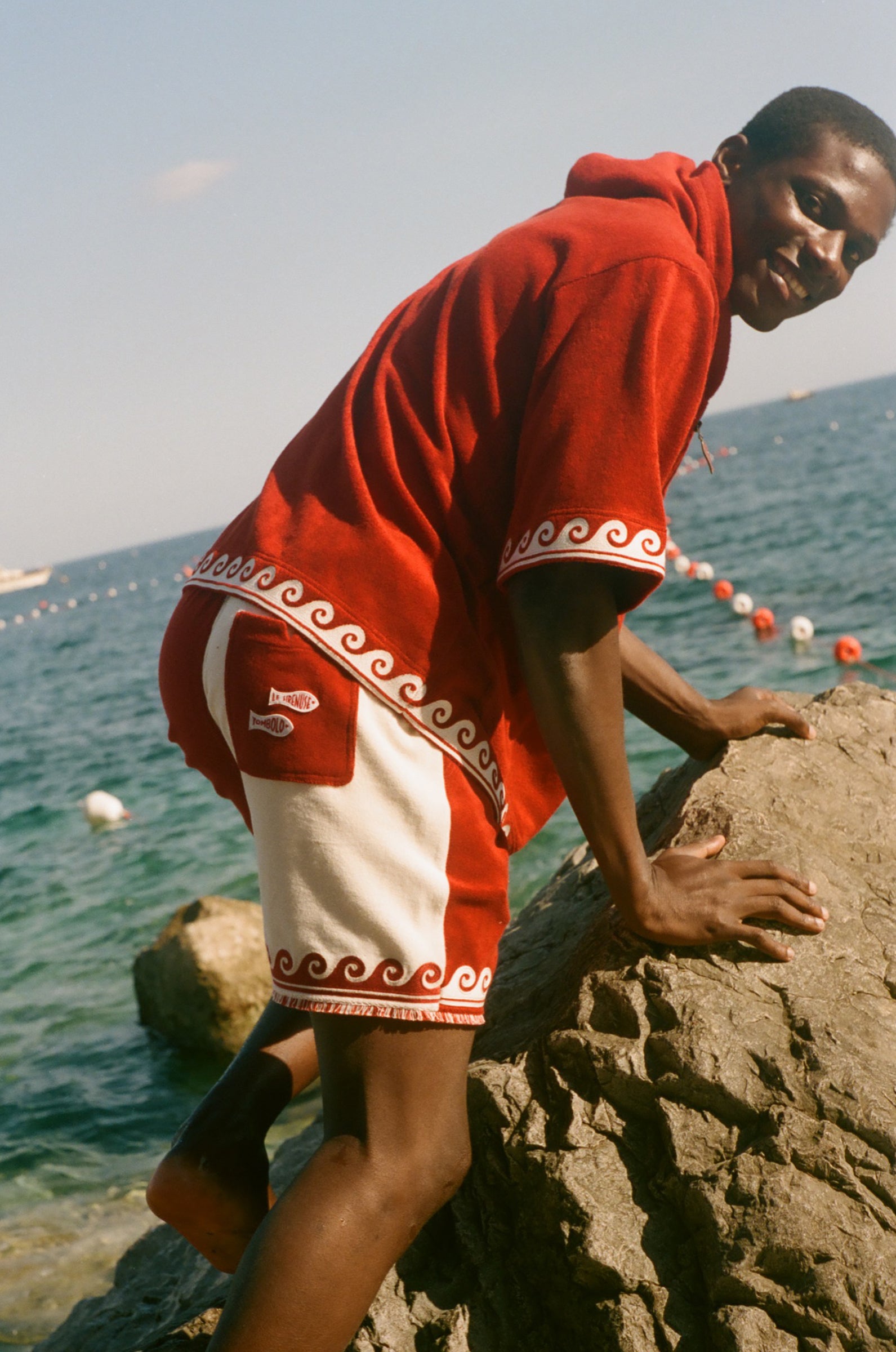 Man climbing on a rock, wearing the Le Sirenuse Beach Towel top. 