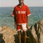 Man wearing Le Sirenuse x Tombolo collection items, standing in front of the ocean. 