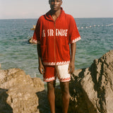 Man wearing Le Sirenuse x Tombolo collection items, standing in front of the ocean. 