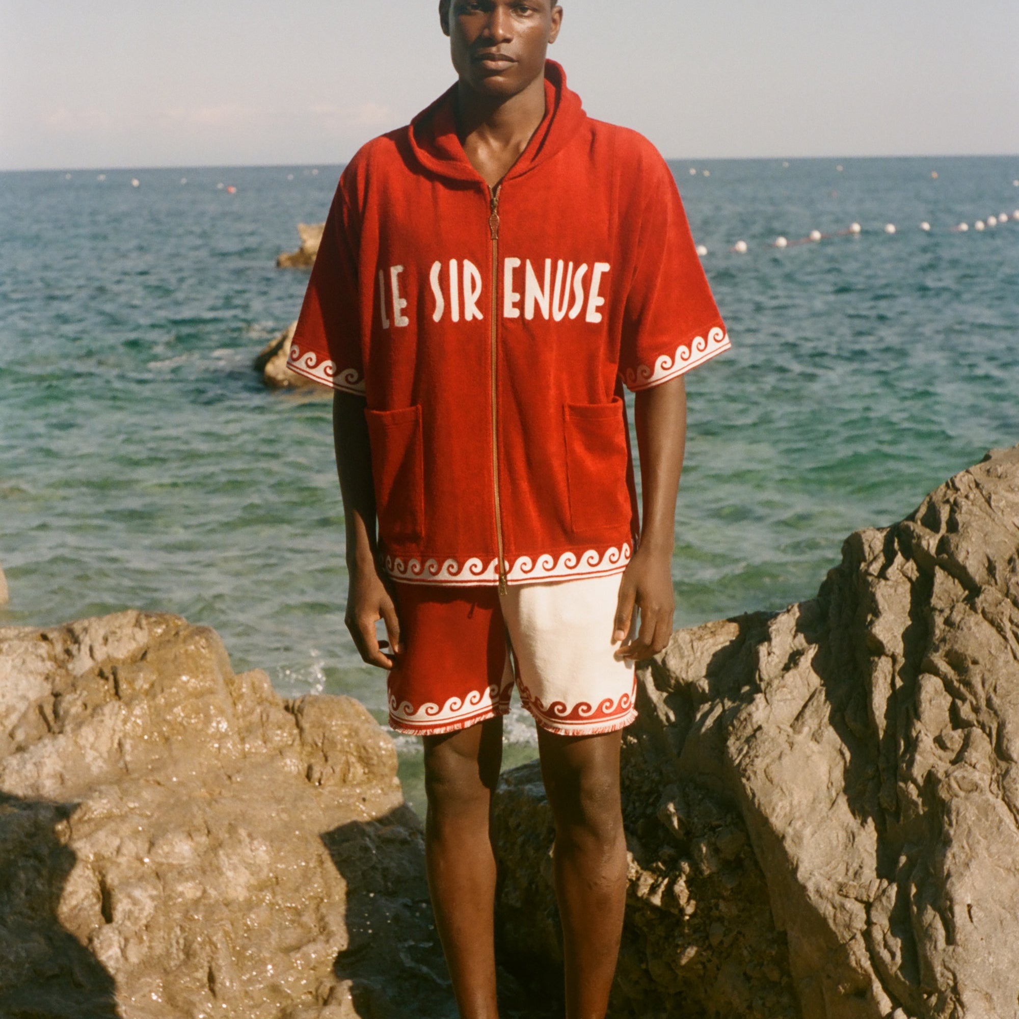 Man wearing Le Sirenuse x Tombolo collection items, standing in front of the ocean. 