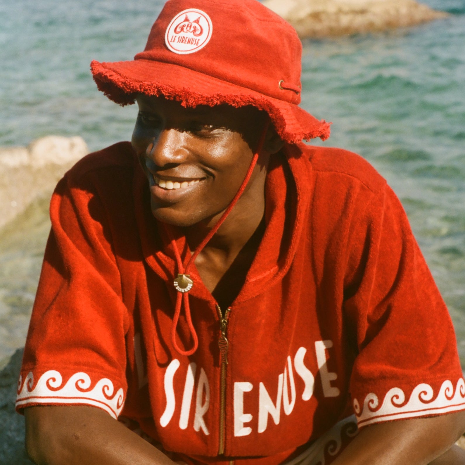 Person wearing a red cabana and cap by a body of water