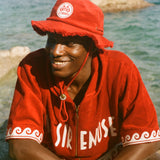 Person wearing a red cabana and cap by a body of water