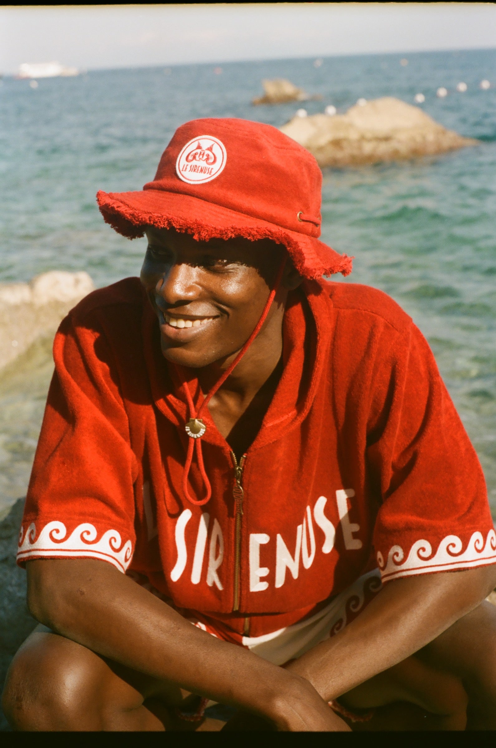 Person wearing a red cabana and cap by a body of water