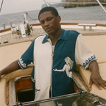 Man wearing Blue and beige Le Sirenuse Late Checkout Cabana, sitting on a boat. 