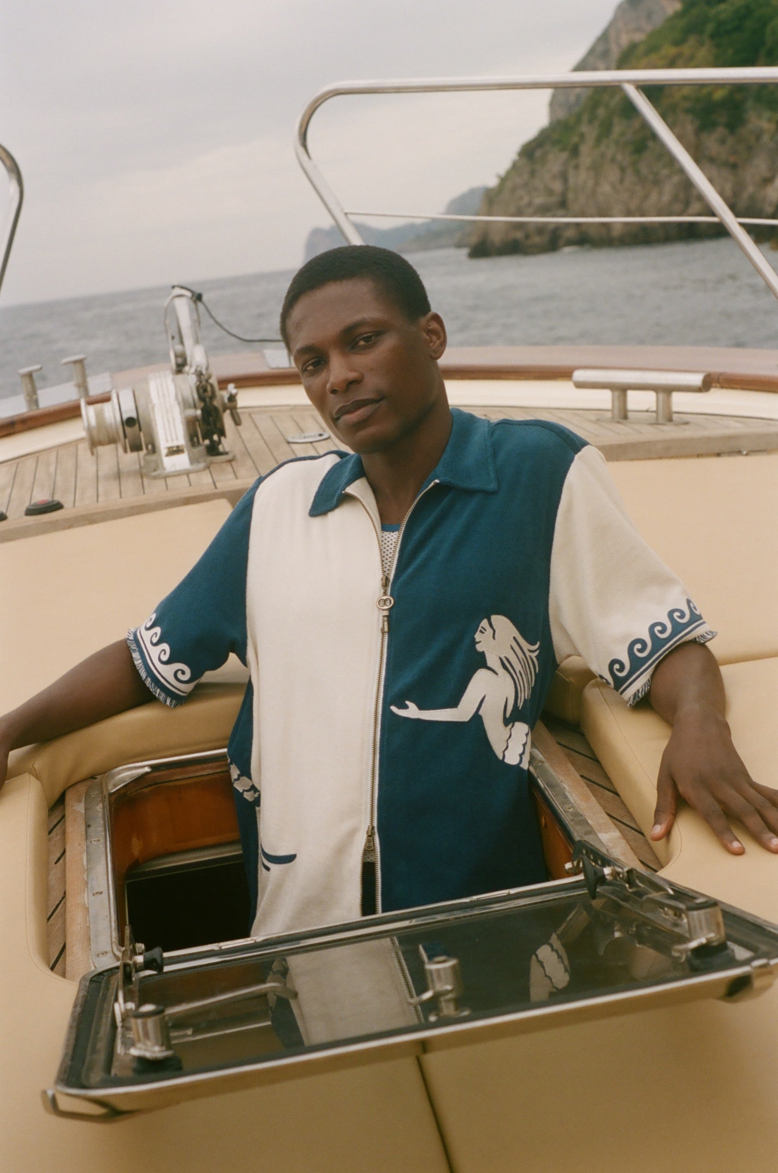 Man wearing Blue and beige Le Sirenuse Late Checkout Cabana, sitting on a boat. 