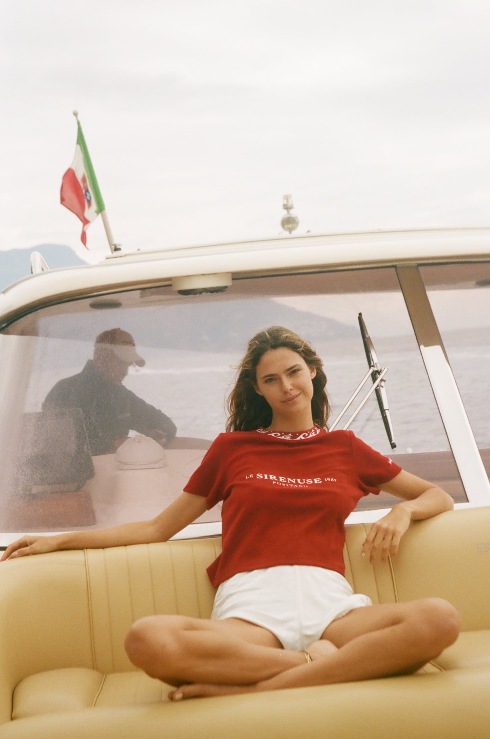 Woman in a red shirt sitting on a boat with an Italian flag in the background