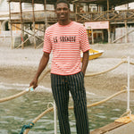 Man standing on a dock wearing a red and white Le Sirenuse striped shirt and black pants.
