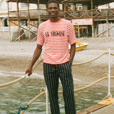 Man standing on a dock wearing a red and white Le Sirenuse striped shirt and black pants.