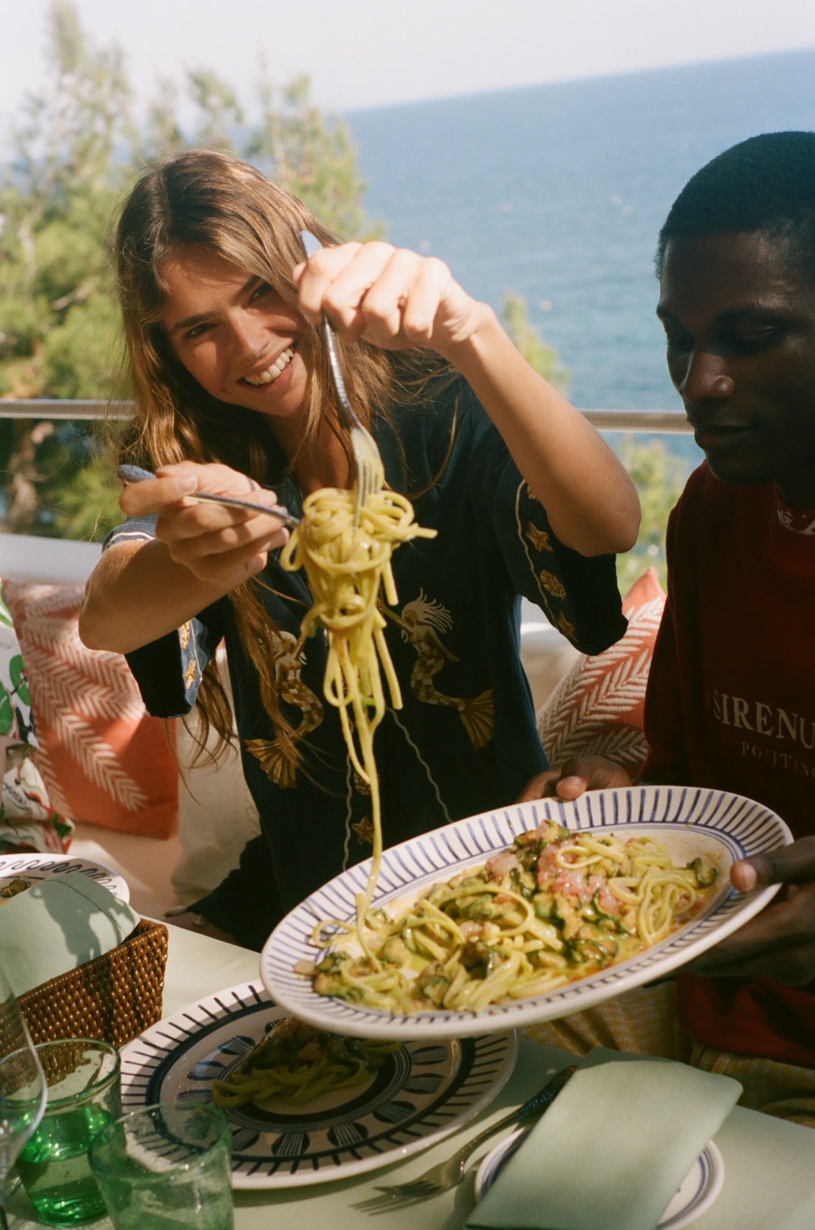 Woman eating noodles outdoors, wearing the Le Sirenuse 'Don't Worry' relaxed crop cut. 