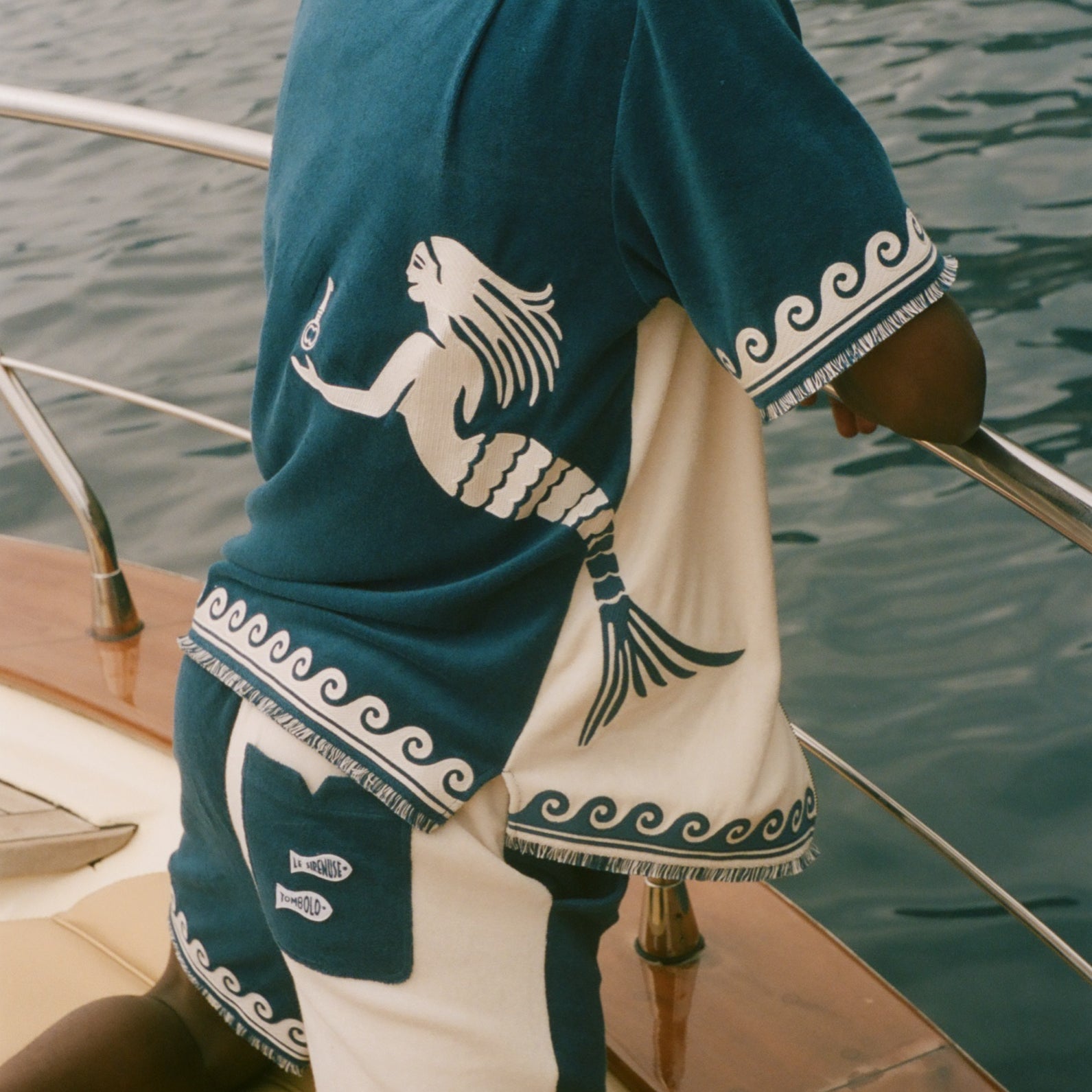 Man wearing Blue Late checkout set, sitting on the edge of a boat. 