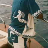 Man wearing Blue Late checkout set, sitting on the edge of a boat. 