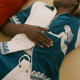 Man wearing a blue and white cabana shirt lying on a wooden floor of a boat.