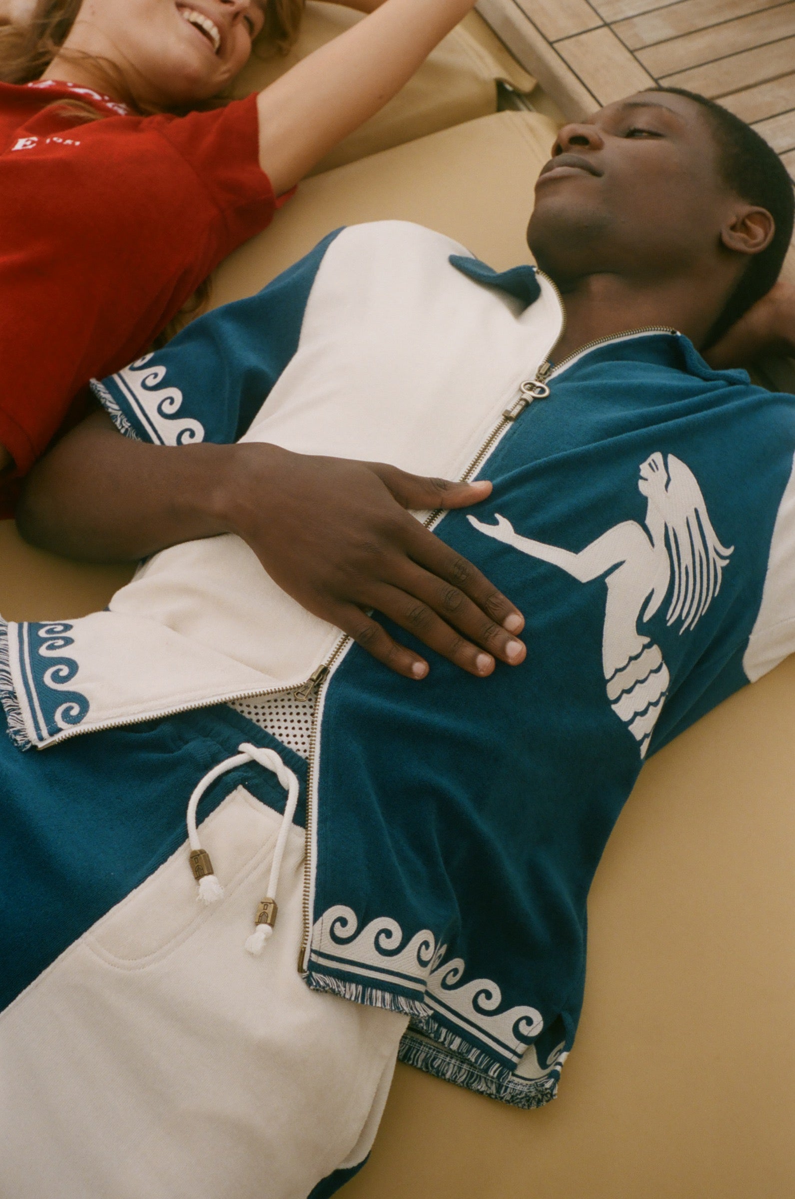 Man wearing a blue and white cabana shirt lying on a wooden floor of a boat.