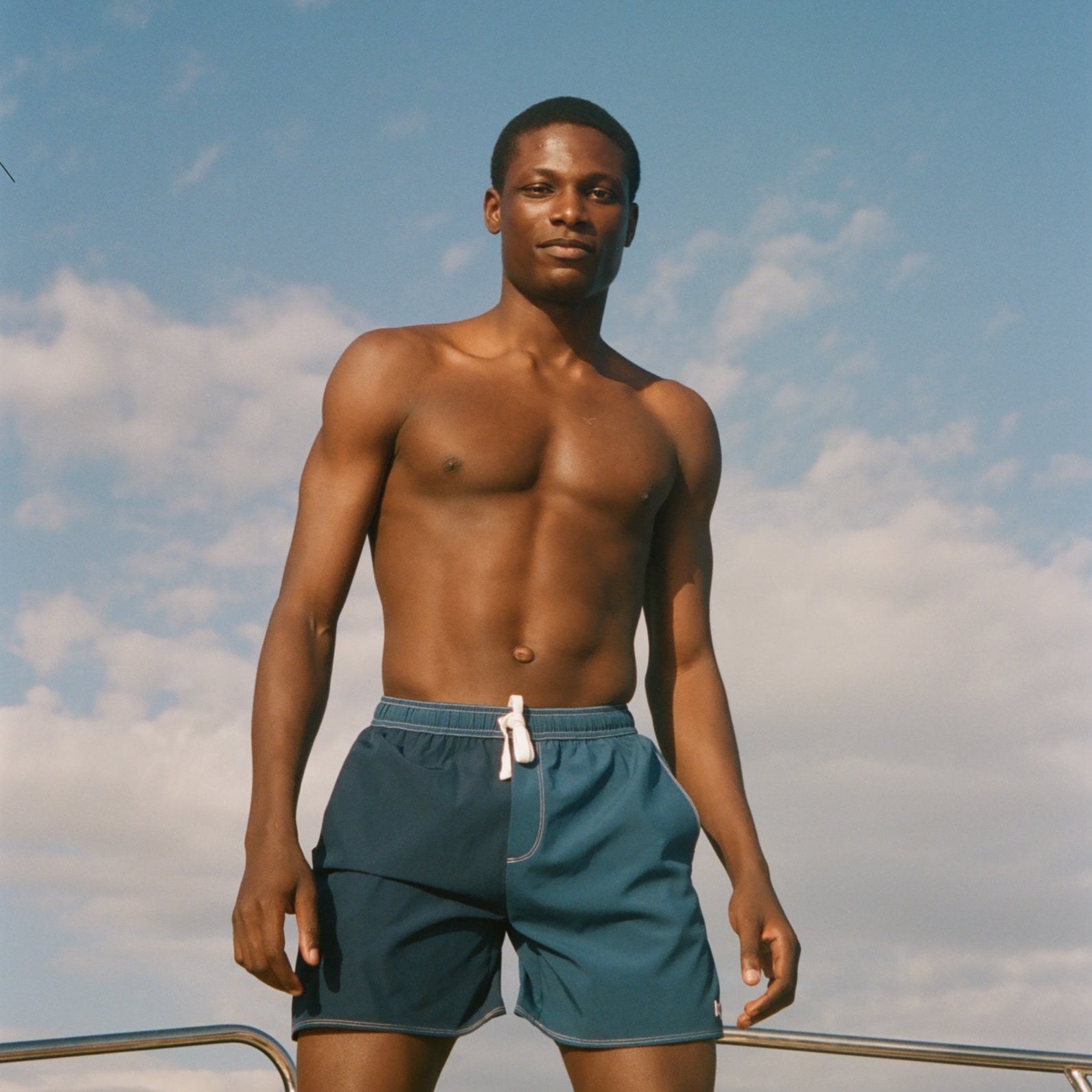 Man in blue shorts standing on a boat with a clear sky background