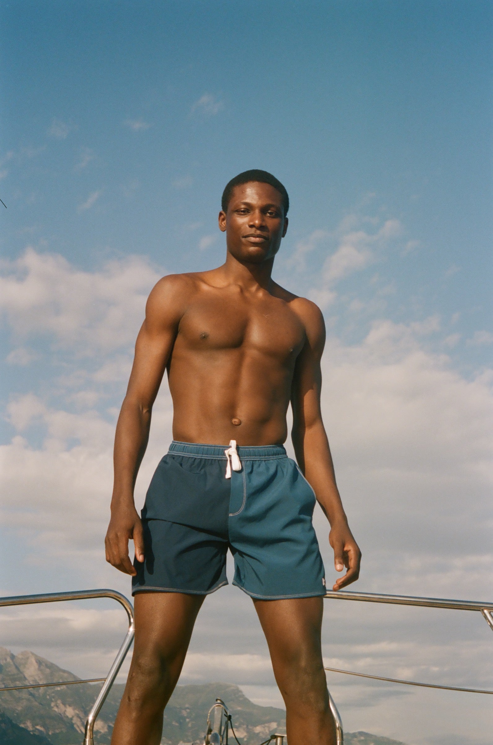 Man in blue shorts standing on a boat with a clear sky background