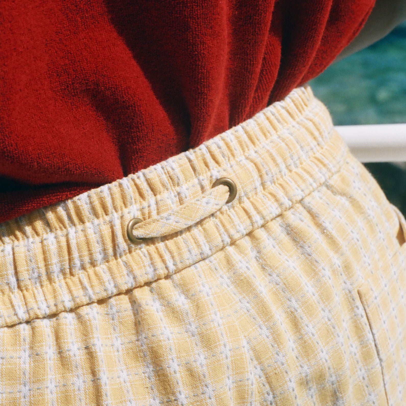 Close-up of a person wearing yellow and white checkered shorts with a gold metal ring closure at the elastic waistband, paired with a red top.
