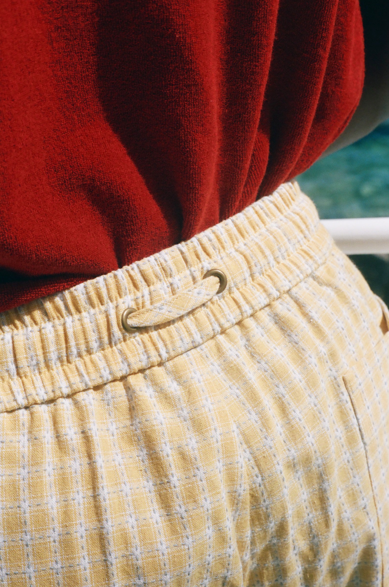 Close-up of a person wearing yellow and white checkered shorts with a gold metal ring closure at the elastic waistband, paired with a red top.